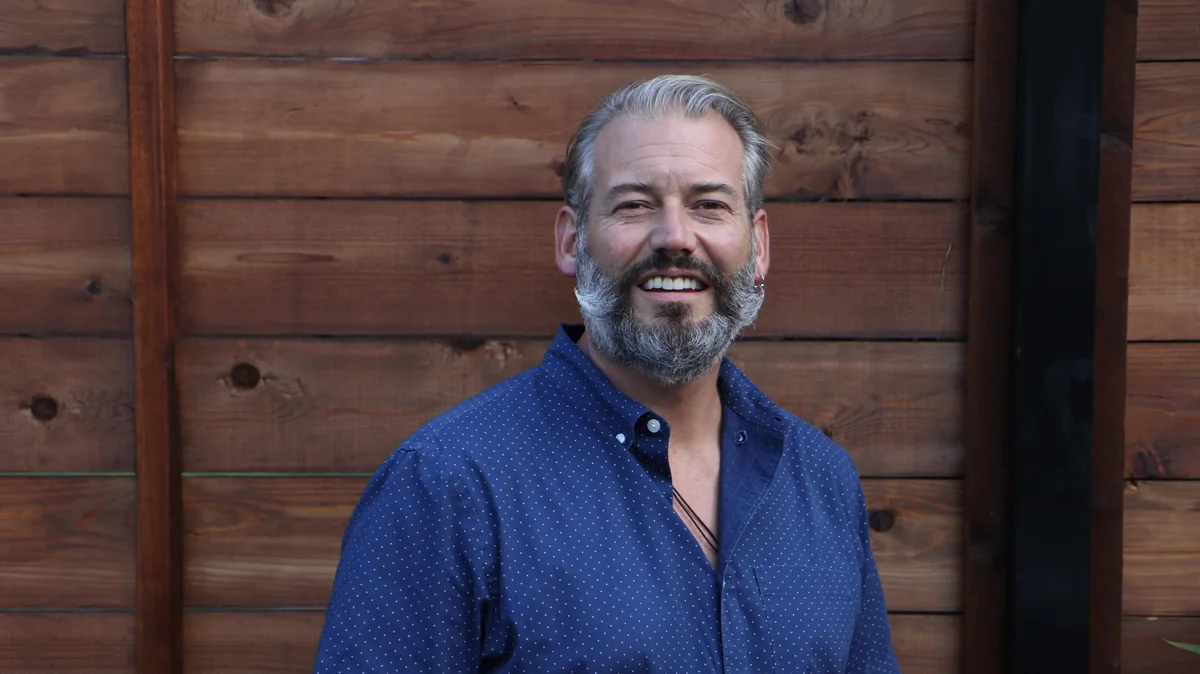 Daniel Lakstins smiling in a navy shirt against a warm wood backdrop